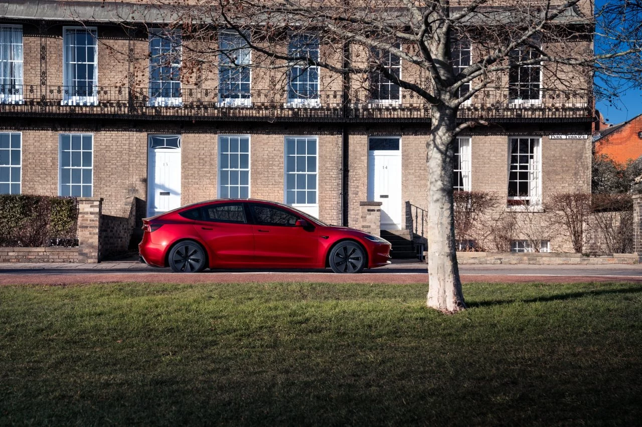 Vista lateral del Tesla Model 3 en entorno urbano, resaltando su línea aerodinámica.