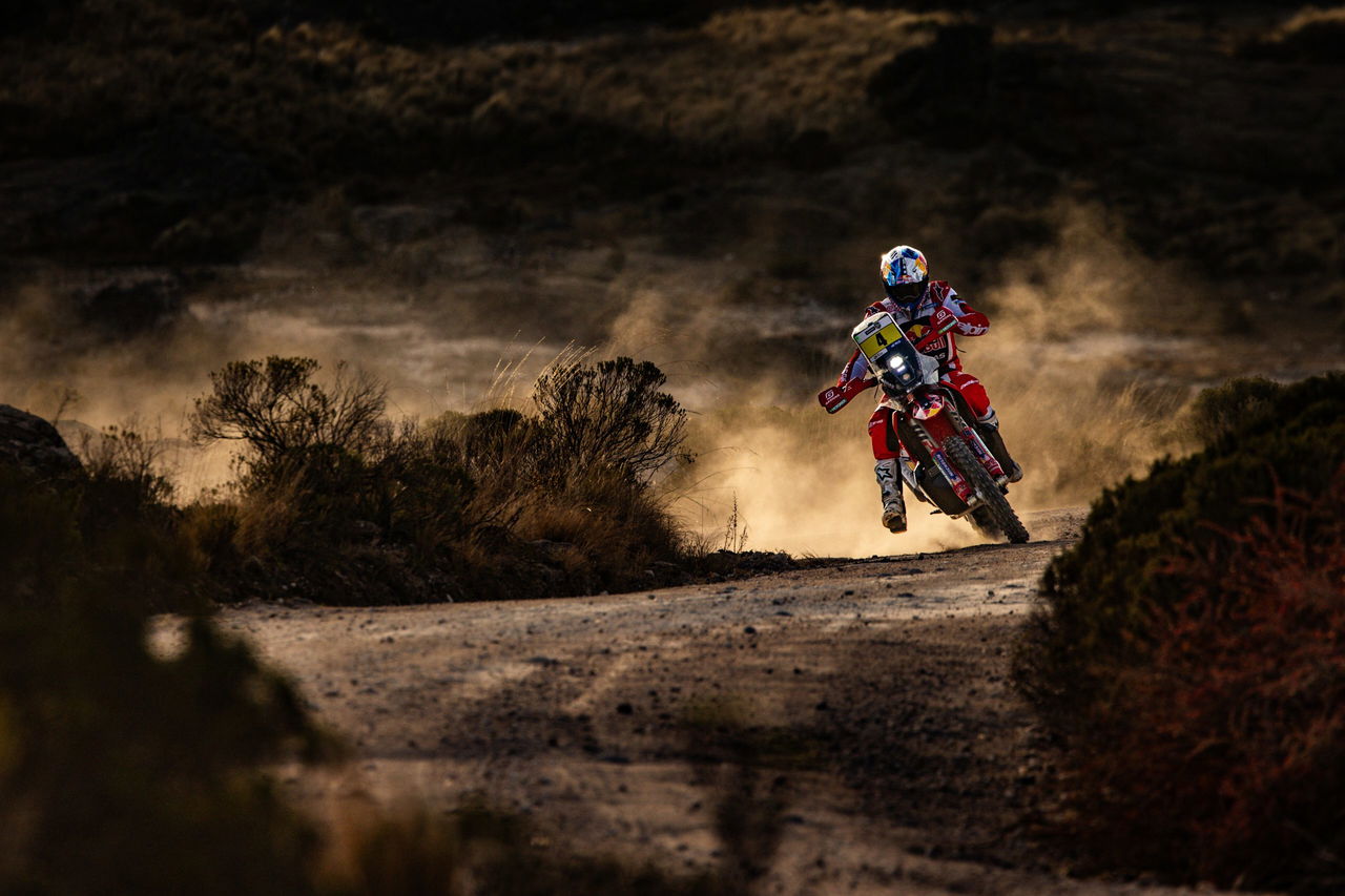 Competidor del Dakar desafiando terreno árido a gran velocidad.