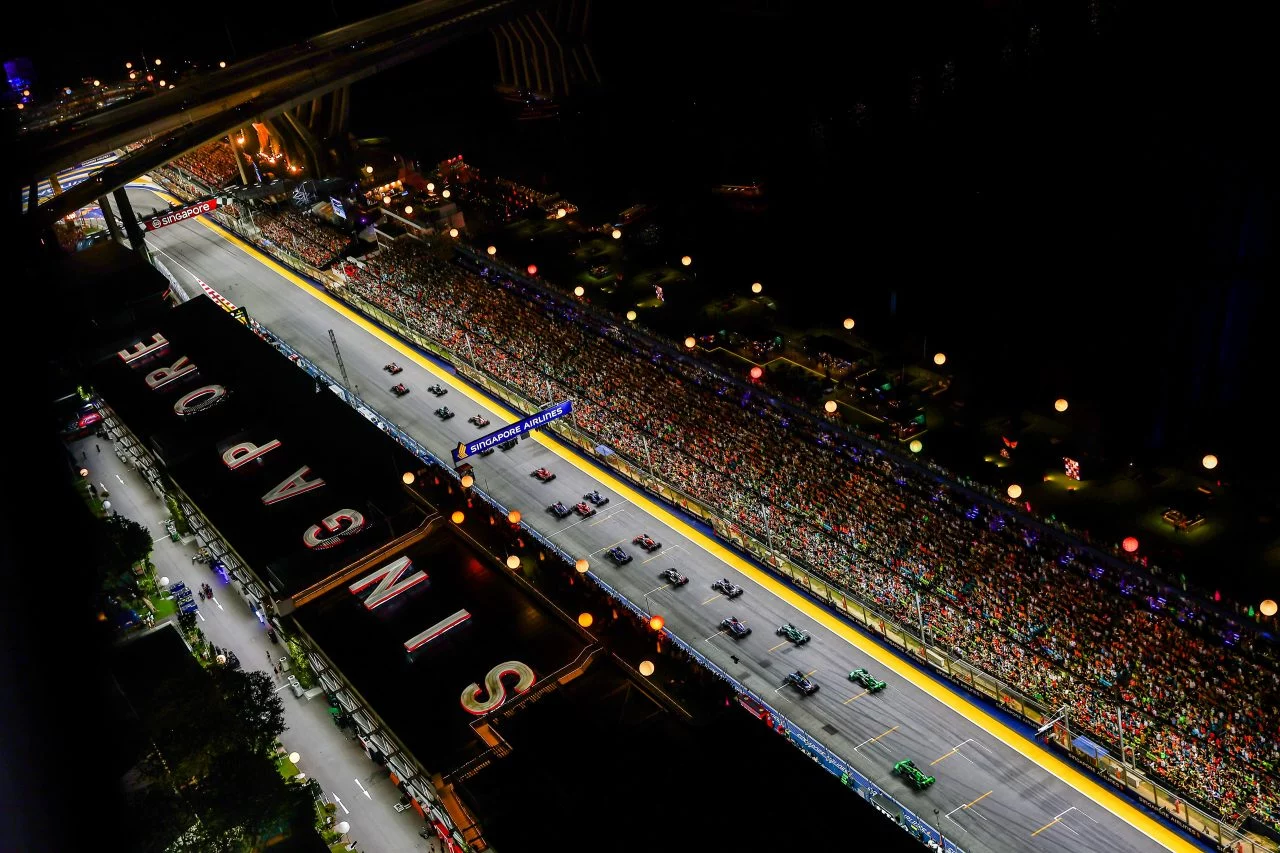 Autos de F1 alineados en parrilla nocturna, iluminación vibrante del circuito.