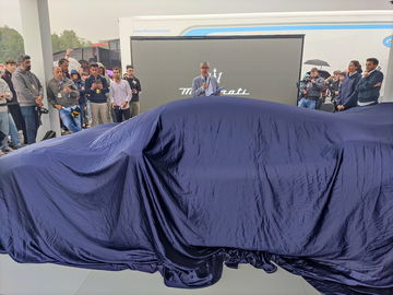 Evento de presentación con un coche cubierto, expectación palpable.