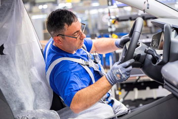 Trabajador en línea de montaje de Volkswagen ajustando el volante.