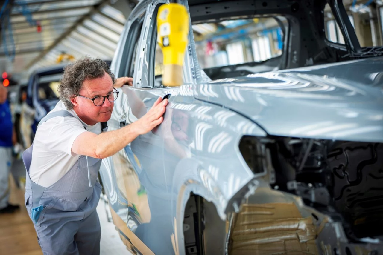 Trabajador ajustando carrocería en línea de producción Volkswagen.