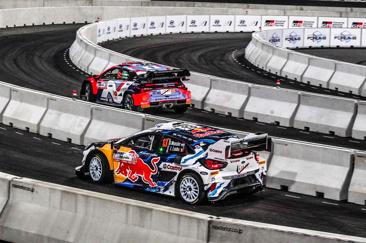 Dos coches de rally compitiendo en un circuito urbano; emoción y velocidad al máximo.