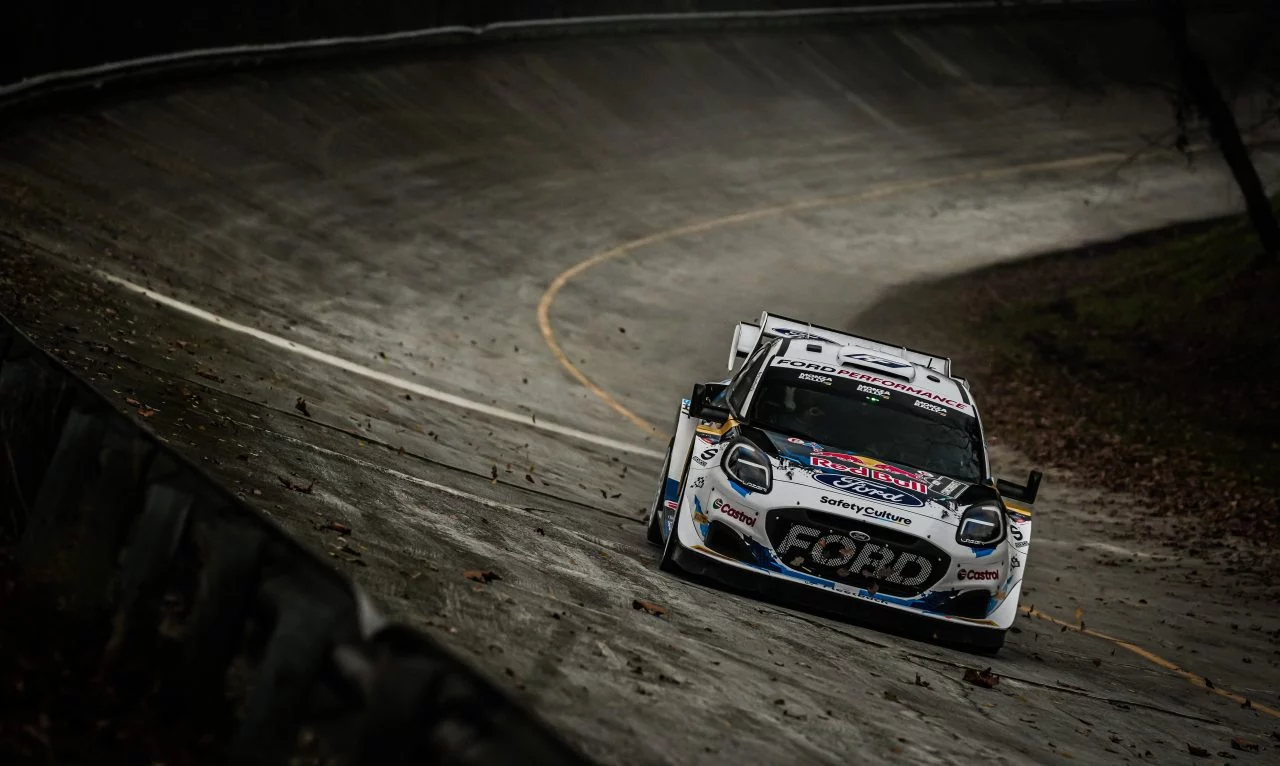 Ford en acción sobre asfalto húmedo en un rally, mostrando su agilidad y diseño aerodinámico.