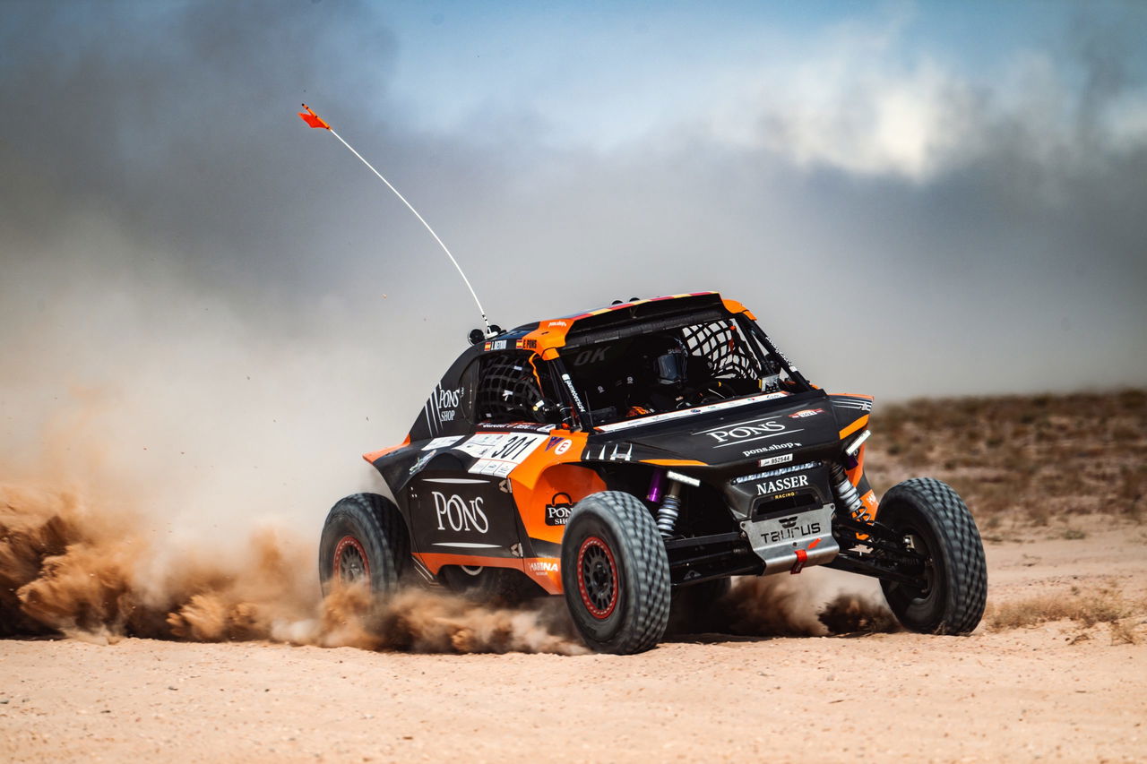 El piloto realiza una espectacular maniobra en el desierto con su vehículo de competición.