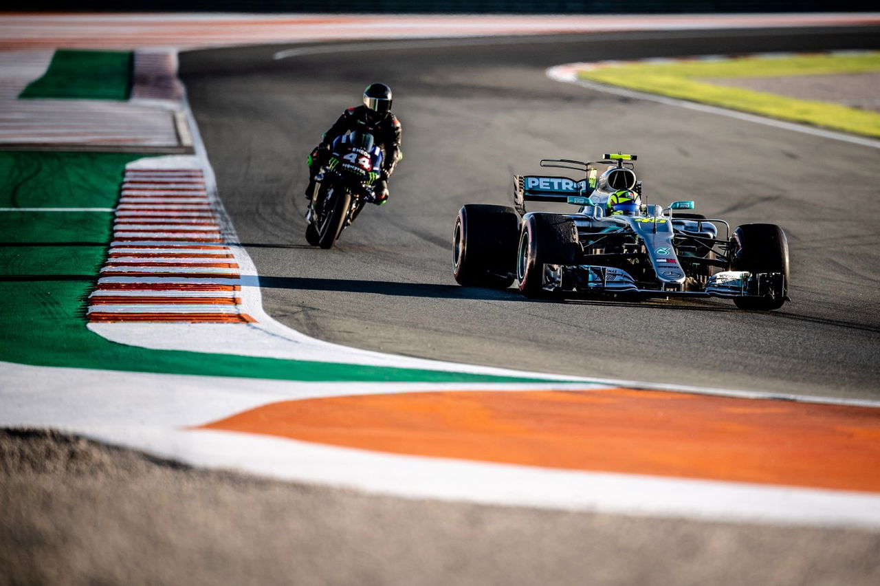 Valentino Rossi y Lewis Hamilton compiten en un circuito, fusionando MotoGP y F1.