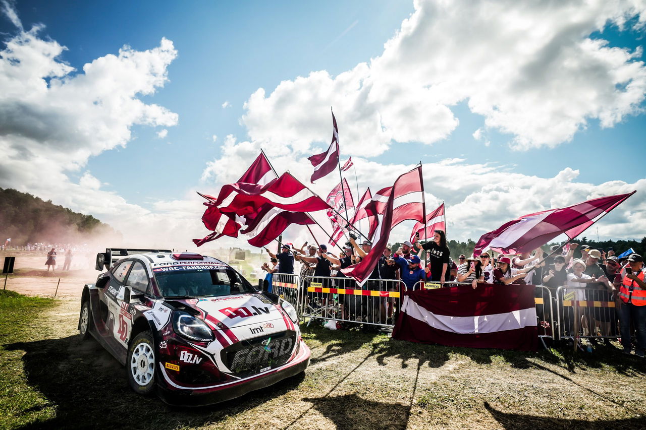 Mārtiņš Sesks a los mandos de su Ford en un rallye, rodeado de aficionados