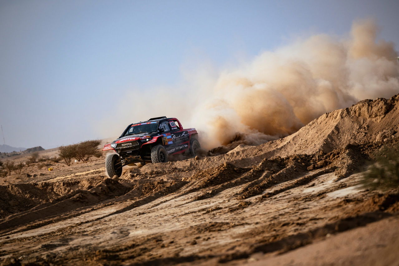 Un coche de rally surca las dunas del desierto, creando una nube de polvo impresionante.