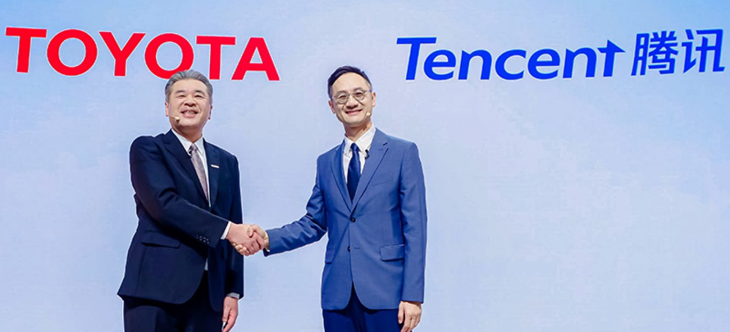 Dos ejecutivos estrechando manos frente a logos de Toyota y Tencent, simbolizando una alianza estratégica.