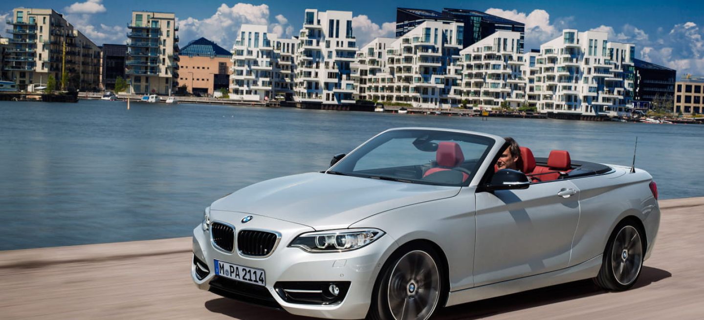 BMW Serie 2 Cabrio en vista delantera lateral, con el techo abajo y un fondo urbano.